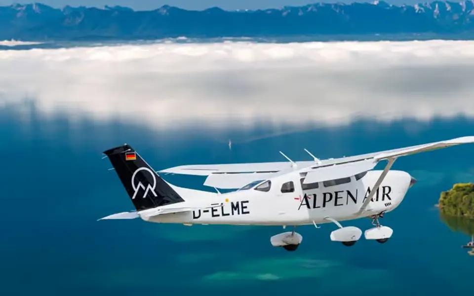 Weißes Flugzeug von ALPEN AIR über einem See vor einer Bergkulisse
